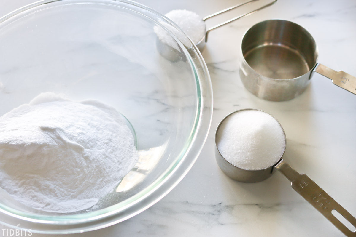 Measuring cups with Fairy Dust Powder near a glass bowl on a marble surface