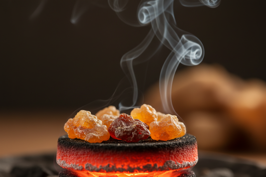Golden frankincense and myrrh resin pieces burning on a glowing charcoal disc with wisps of white aromatic smoke rising against a dark background
